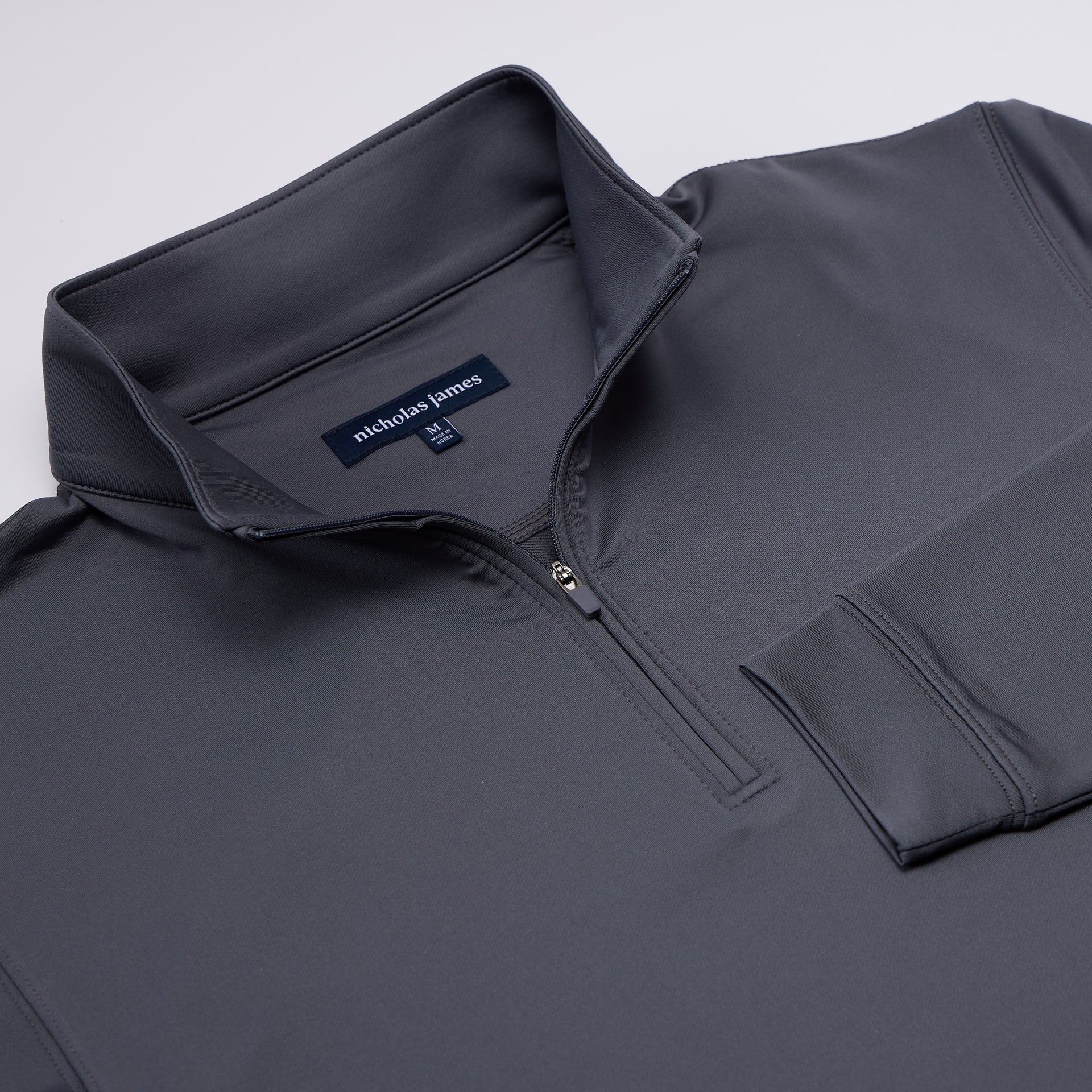 Gray pullover with nicholas james label on a light gray background