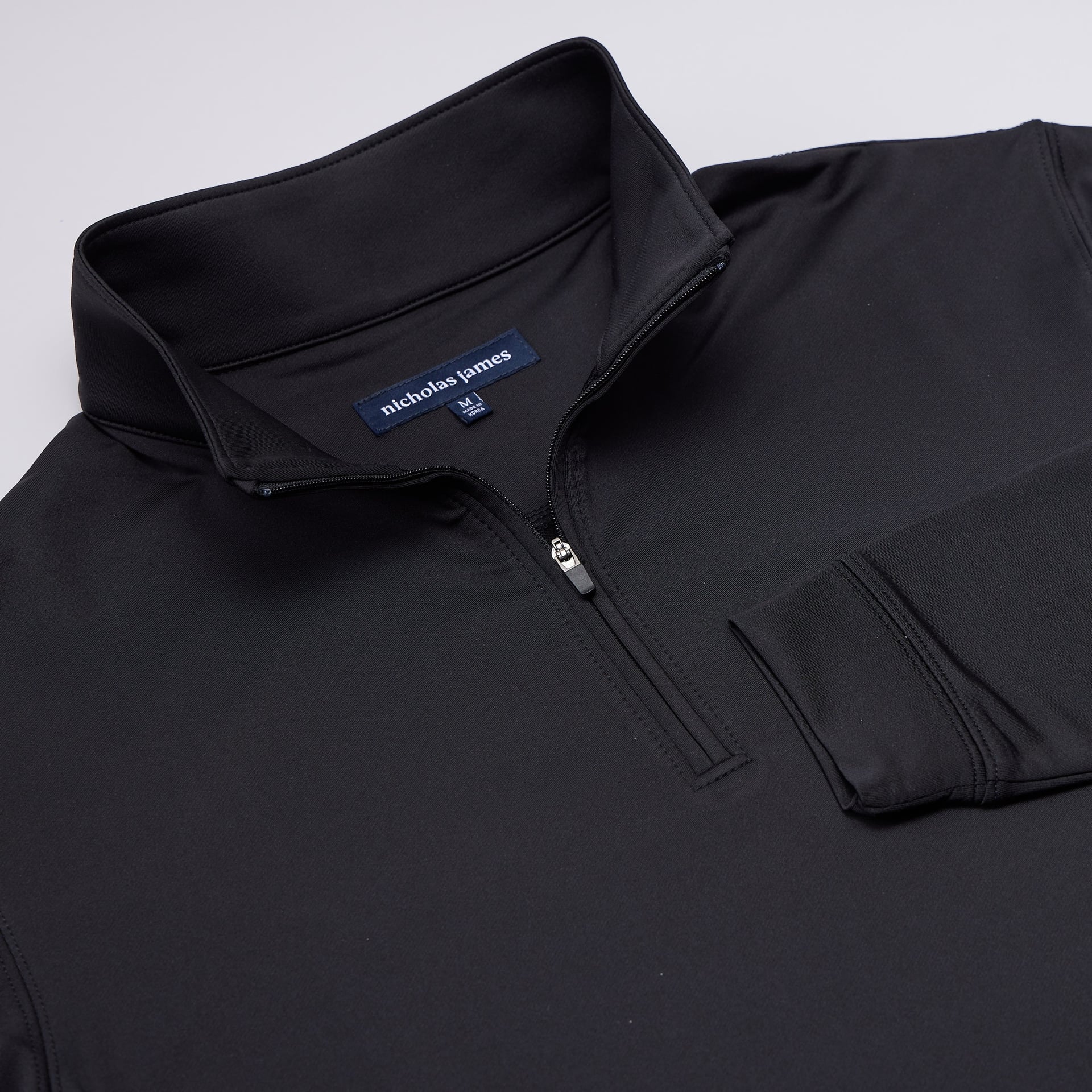 Black quarter-zip sweatshirt with nicholas james logo on a light gray background