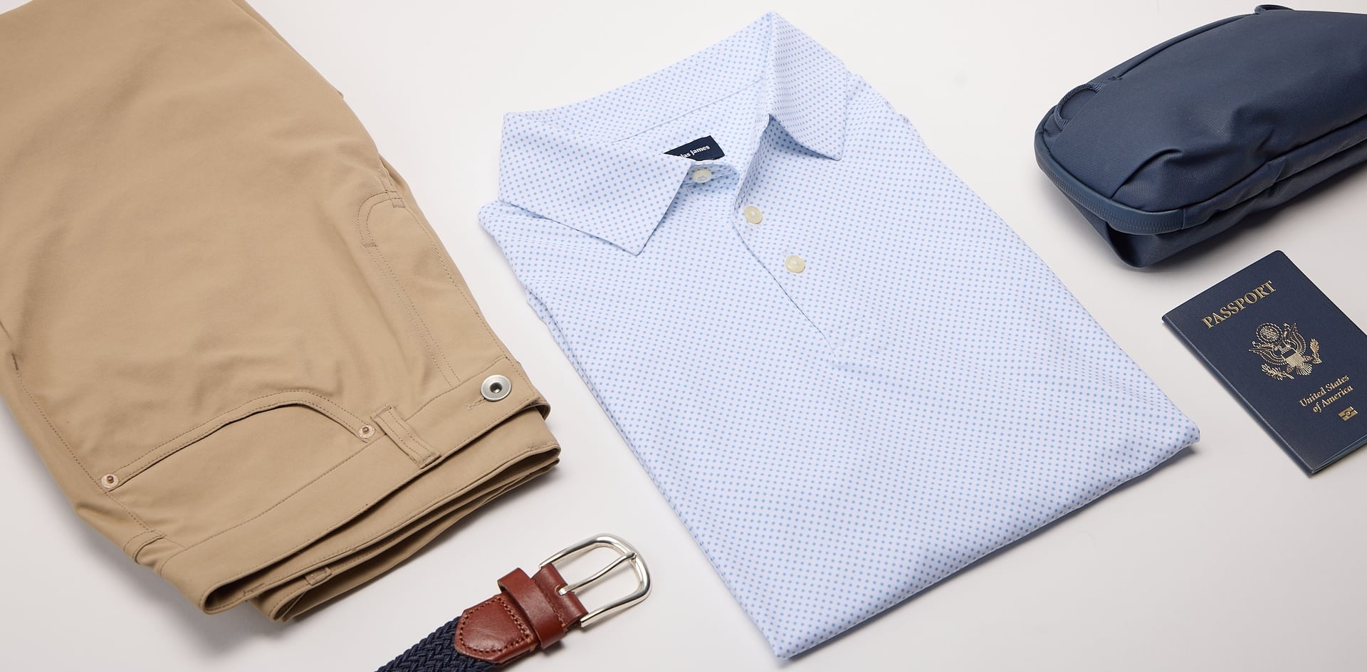 Light blue pin dot shirt, beige pants, brown belt, and navy suitcase on a light gray background