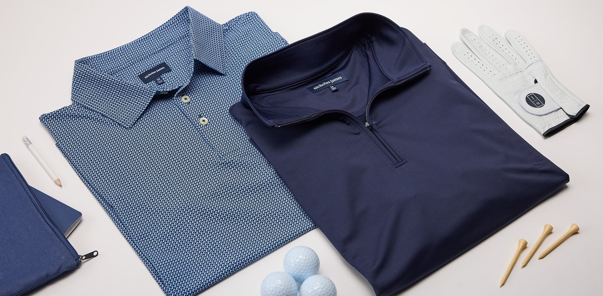 Two blue polo shirts, a golf glove, golf balls, and golf tees on a white surface.